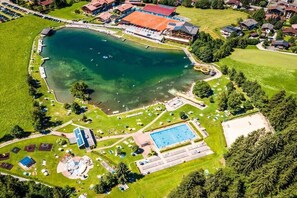 Eine Vogelperspektive auf ein Anwesen am Seeufer mit Schwimmbad, Tennisplätzen und einem großen Gebäude mit rotem Dach.