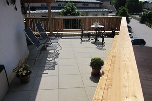 Ein Balkon mit Holzgeländer, einem Tisch, Stühlen und Topfpflanzen.
