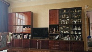 Una habitación con un armario de madera que contiene varios objetos, un televisor y una ventana con cortinas.