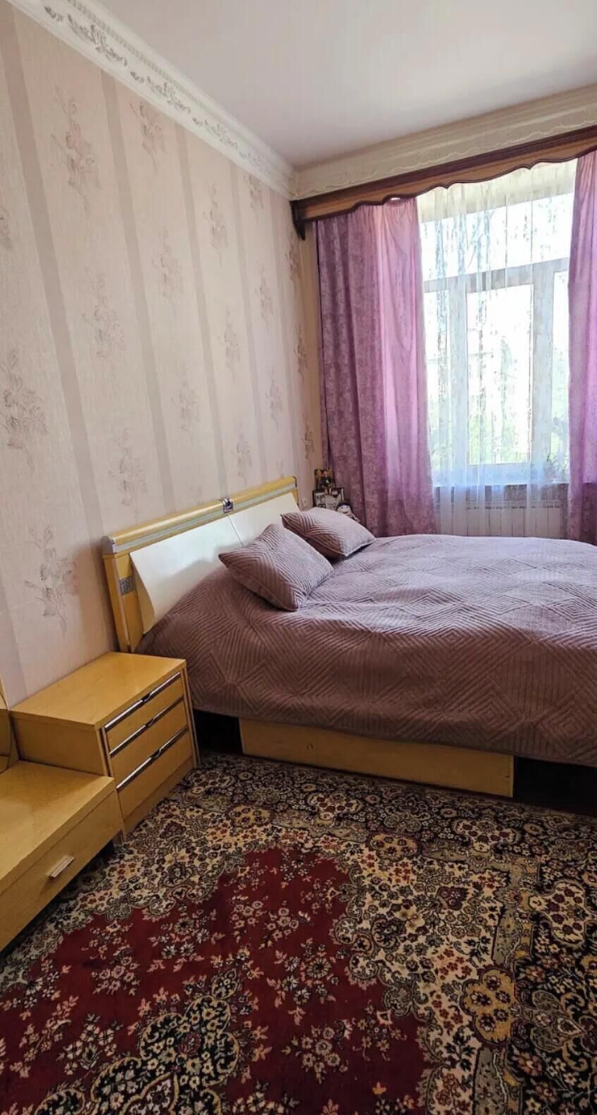 A bedroom with a bed, a nightstand, a dresser, and a patterned carpet.