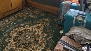 Una habitación con cama, armario, escritorio, lámpara y ventana con cortinas.