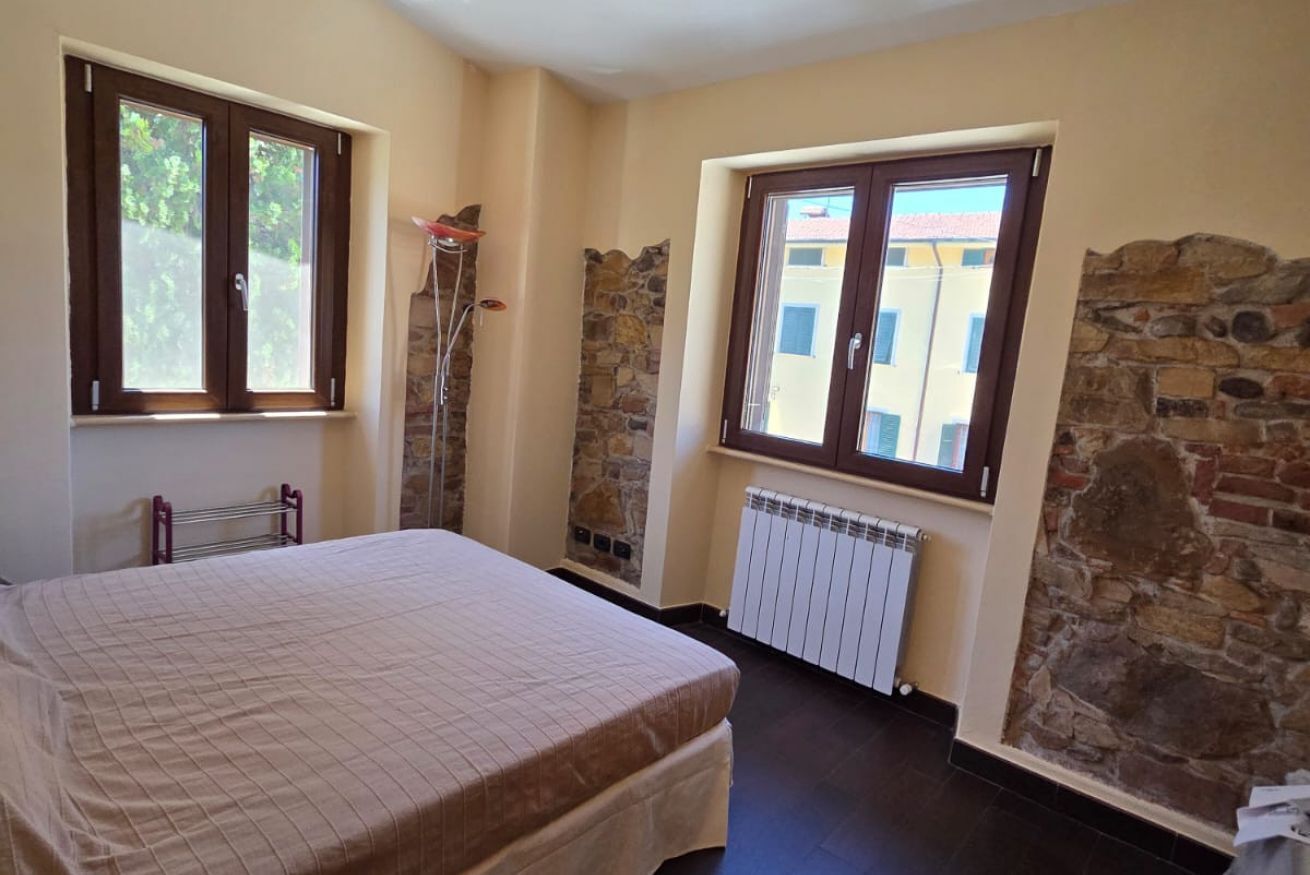 Ein Schlafzimmer mit einem Bett, zwei Fenstern, einer Heizung und Steinwänden.