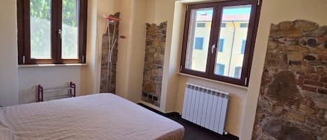 Una camera da letto con un letto, due finestre, un termosifone e pareti in pietra.