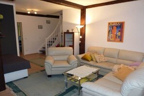 Un salon comprenant un canapé, des fauteuils, une table basse et un escalier menant à une autre pièce.