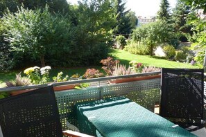 Ein Balkon mit einer grünen Sitzgelegenheit im Freien, umgeben von üppiger Bepflanzung und einem gepflegten Garten.