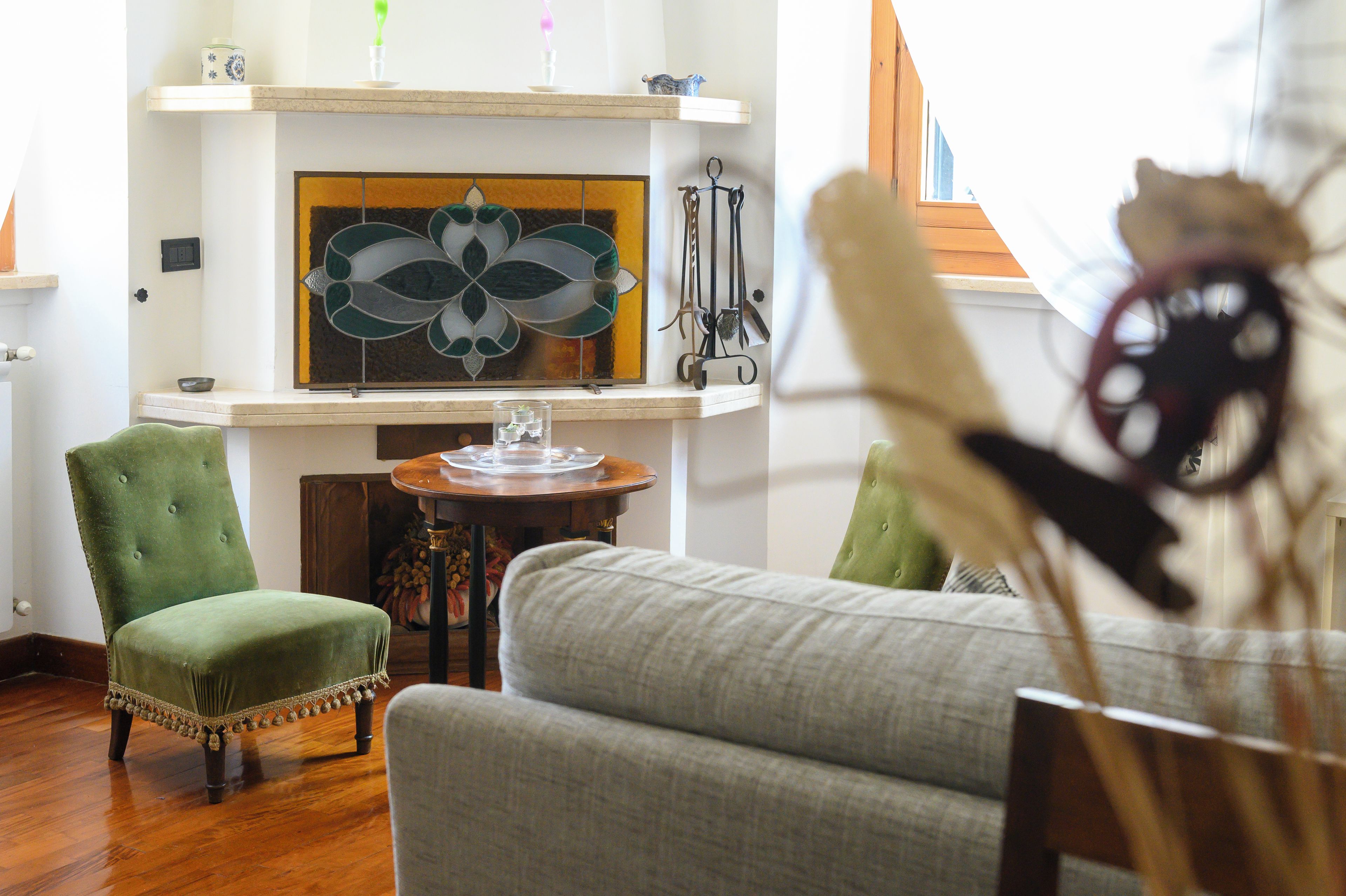 A living room with a fireplace, green armchairs, a round wooden table, and a decorative glass piece.