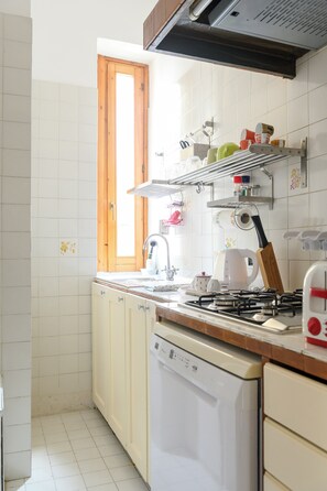Eine Küche mit weißen Schränken, einem Geschirrspüler, einem Herd und einem Fenster mit Holzrahmen.