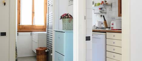 A narrow hallway leading to a kitchen with a refrigerator, a window, and a sink.