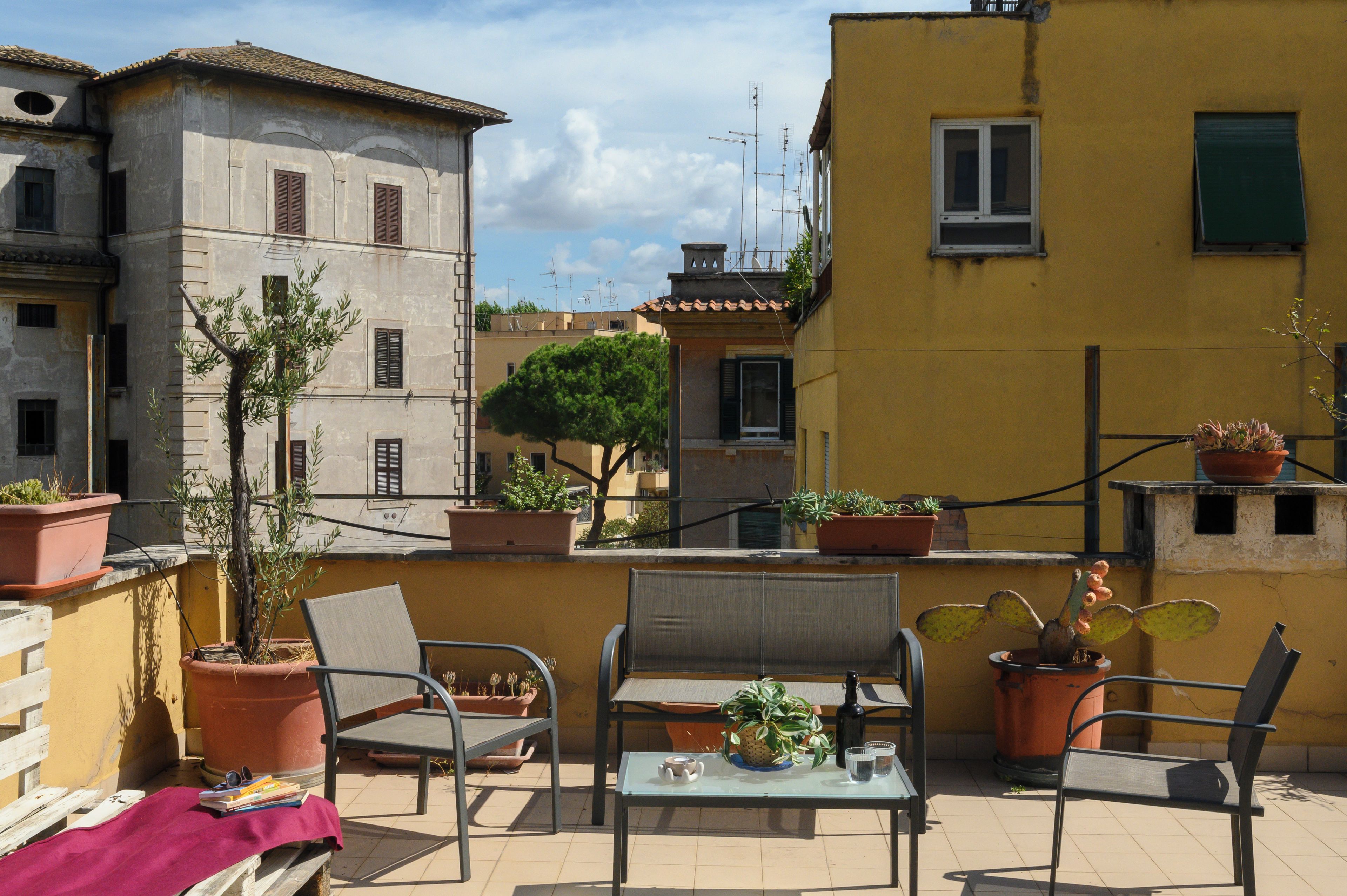 En terrasse med udendørs møbler, plantekasser og udsigt til omkringliggende bygninger.