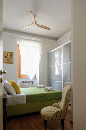 A bedroom with a bed, a chair, a ceiling fan, a window with curtains, and a radiator. - Garbatella: Apartment with a terrace near the metro (Roma)