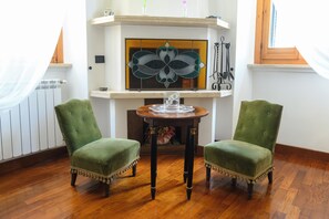A room with two green upholstered chairs, a wooden table with a glass top, and a fireplace with a decorative glass piece above it. - Garbatella: Apartment with a terrace near the metro (Roma)