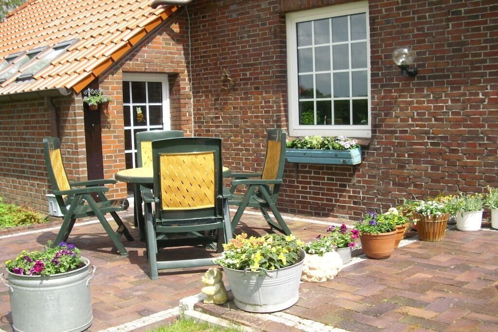 A brick building with a tiled roof, a window, and a patio area with outdoor furniture and potted plants.