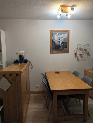A dining area with a wooden table and chairs, a coffee machine, and a framed picture on the wall. - Valloire Apartment: 1-Bedroom / Sleeps 4 Right at the base of the slopes, with a heated pool and parking (Valloire)
