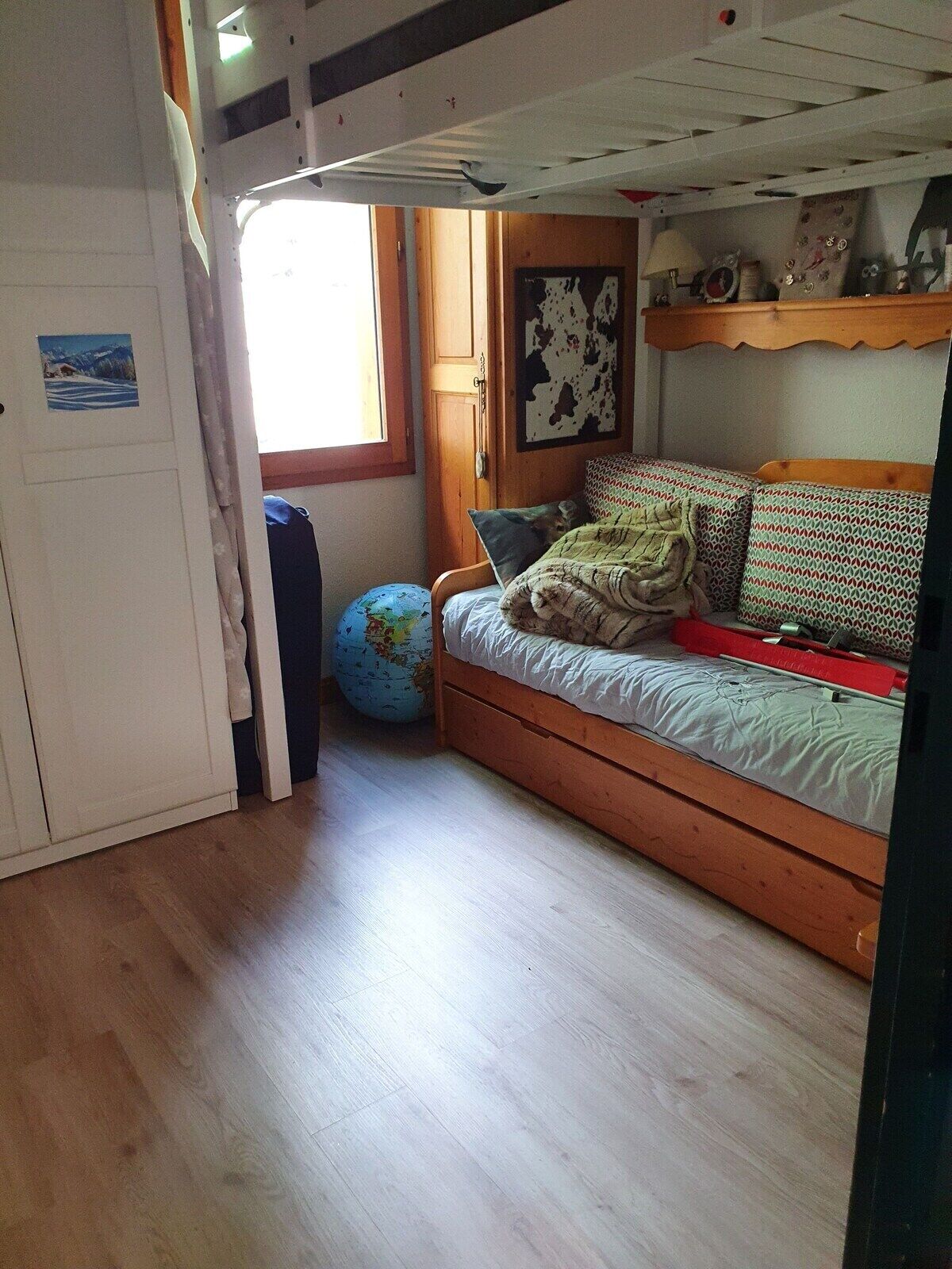 Een knus kamertje met een houten bed, een wereldbol en een deur naar een andere kamer.
