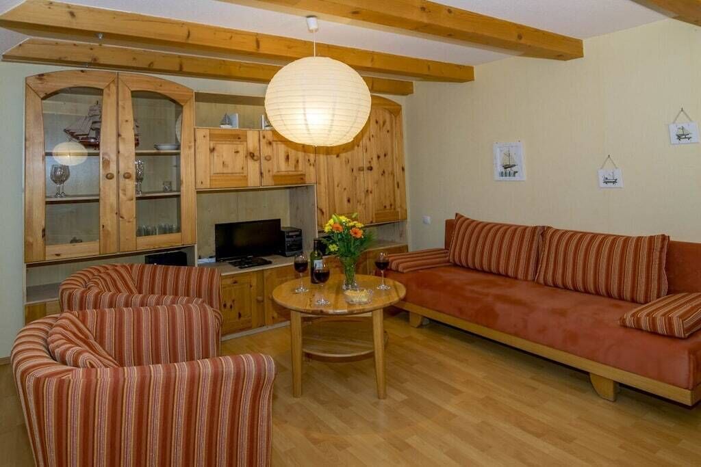 Una sala de estar acogedora con sofás a rayas, una mesa de comedor de madera con un florero y una zona de cocina con armarios de madera y un colgador de techo.