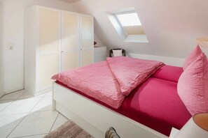 Ein Schlafzimmer mit Bett, Schrank, Schreibtisch und Dachfenster.
