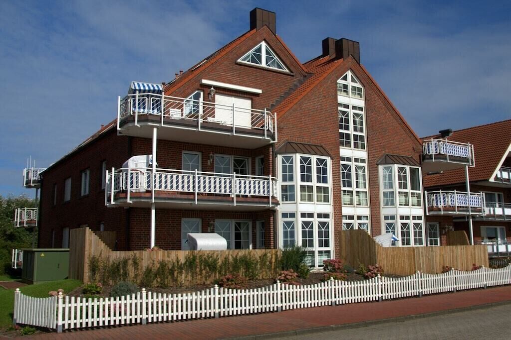 A two-story brick house with a balcony on the upper floor, a chimney, and a white picket fence.