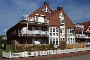 A two-story brick house with a balcony on the upper floor, a chimney, and a white picket fence. - Holiday apartment in Juist with swimming pool (Juist)