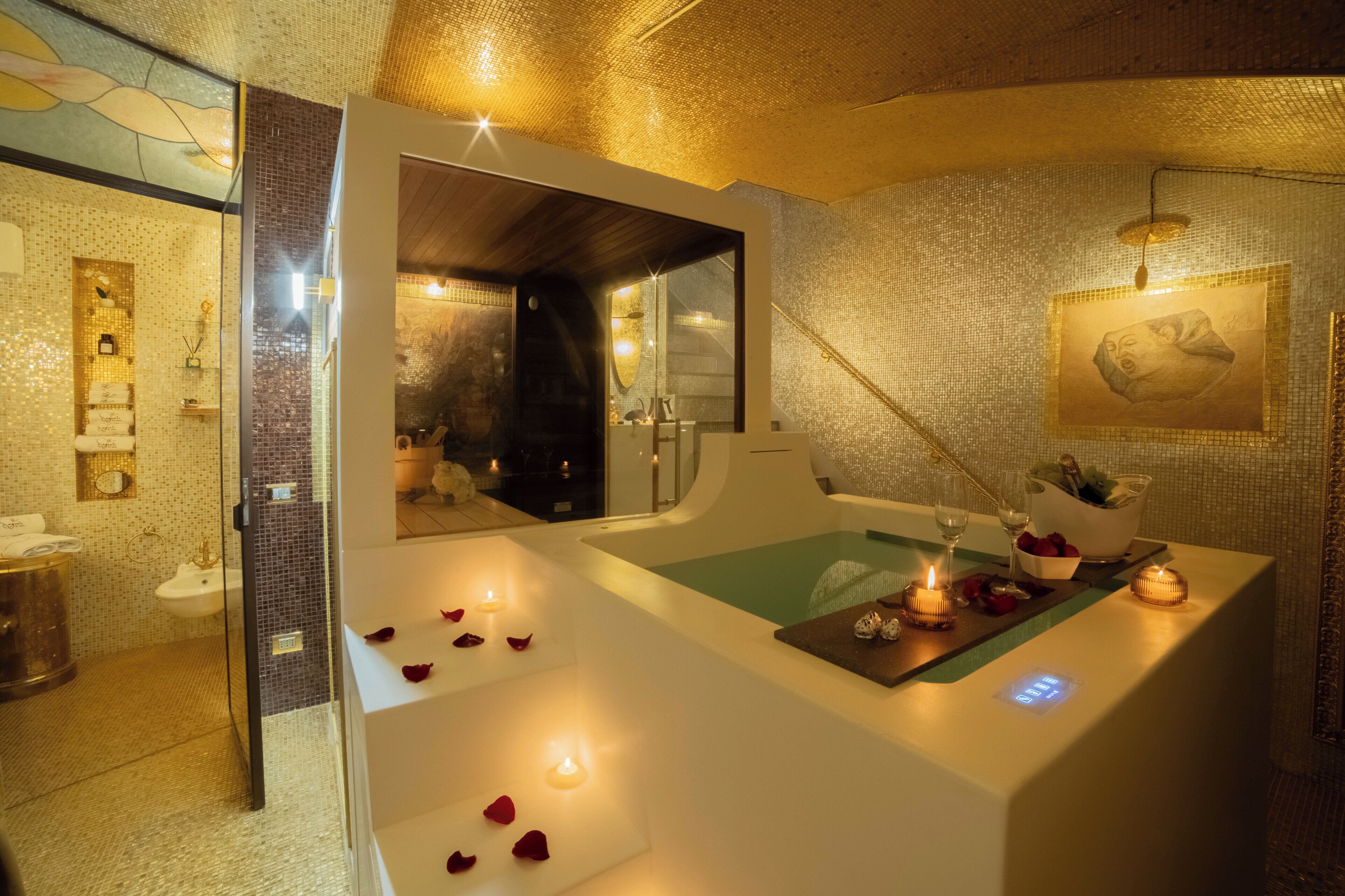 A spa room with a bathtub, a mirror, and a small table with candles and flowers.