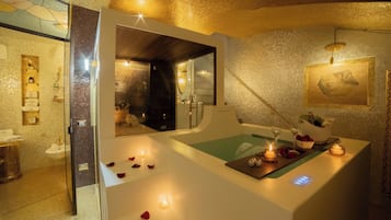 A spa room with a bathtub, a mirror, and a small table with candles and flowers.