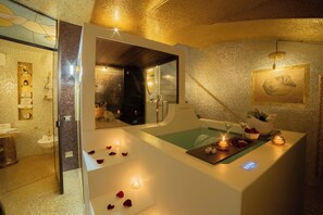 A spa room with a bathtub, a mirror, and a small table with candles and flowers.