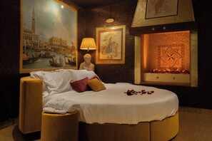 A hotel room with a large bed, a nightstand, a lamp, and a fireplace.