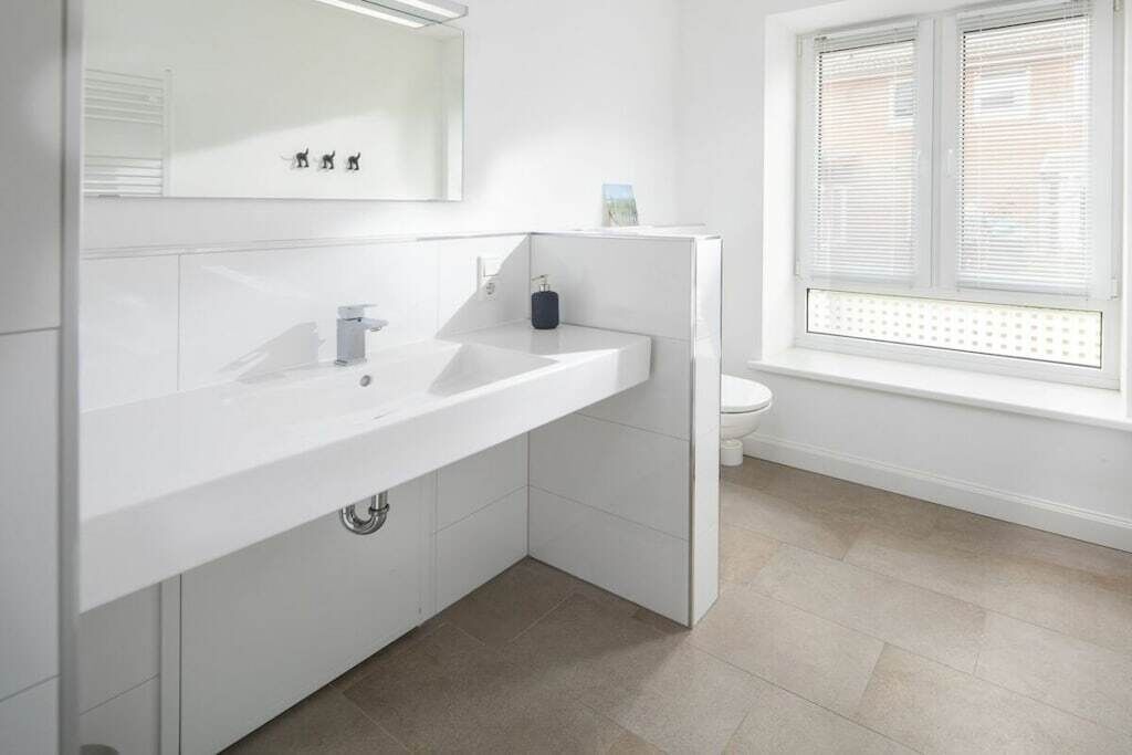 Een moderne badkamer met een witte wastafel, spiegel en toilet.