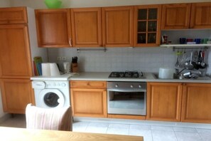 A kitchen with wooden cabinets, a washing machine, a stove, and a sink. - Holiday home with 2 bedrooms (St. Pol de Léon)