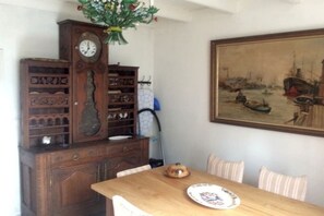 Uma sala de jantar com uma mesa de madeira, cadeiras, um relógio e um quadro na parede.