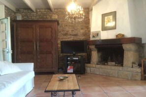 A living room with a stone fireplace, a television, and a white sofa. - Holiday home with 2 bedrooms (St. Pol de Léon)