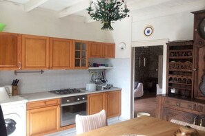 A kitchen with wooden cabinets, a stove, and a dining area with a table and chairs. - Holiday home with 2 bedrooms (St. Pol de Léon)