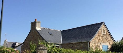 A stone building with a sloped roof, a chimney, and a small window.