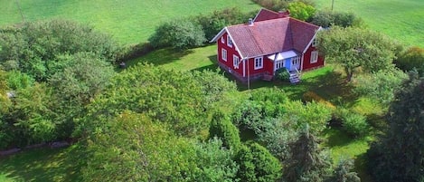 A red house with a red roof surrounded by green fields and trees.