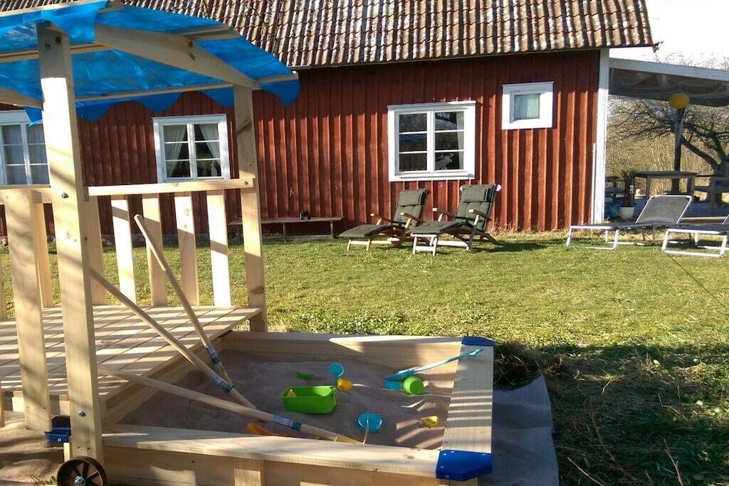 A wooden play structure with a shaded area, a red building with windows, and outdoor seating.