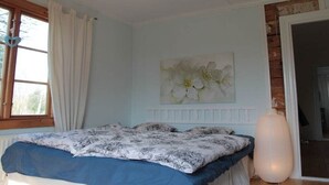 Una camera da letto con un letto, una finestra con tende, un'opera d'arte appesa al muro e una porta che dà su un'altra stanza.