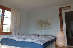 A bedroom with a bed, a window with curtains, a wall-mounted artwork, and a door leading to another room. - Holiday home in Torsas with swimming pool (Torsas)