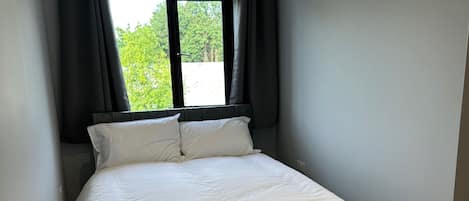 Un dormitorio con cama, ventana con cortinas y vista a zonas verdes.
