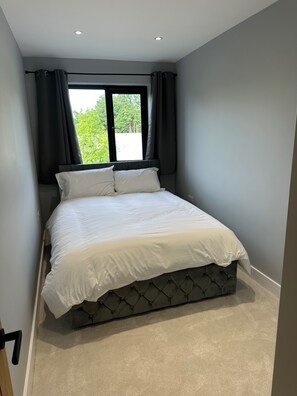 A bedroom with a bed, a window with curtains, and a view of greenery outside. - Apartment Sleeps 4 - Free Parking & Wifi (London)