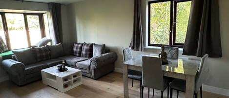 Amplia sala de estar con un conjunto de sofás, una mesa de comedor con sillas y un ventanal con cortinas.