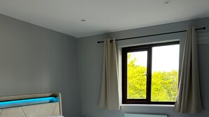 Une chambre à coucher avec un lit, une fenêtre avec des rideaux et une vue sur la verdure à l’extérieur.