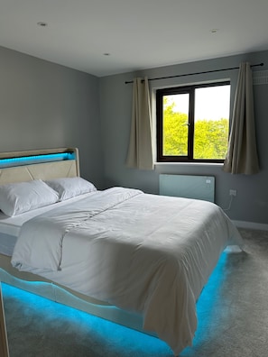 Ein Schlafzimmer mit Bett, einem Fenster mit Vorhängen und Blick auf Grünfläche.