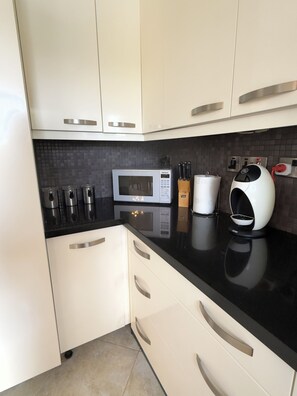 Eine moderne Küche mit weißen Schränken, einer schwarzen Arbeitsplatte, einer Mikrowelle, einer Kaffeemaschine und einem Messerblock.