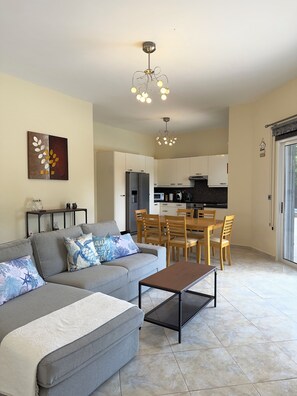 A modern living room with a sofa, coffee table, and dining area with chairs. - Family Villa With Large Pool, Home Away From Home (Pegeia)
