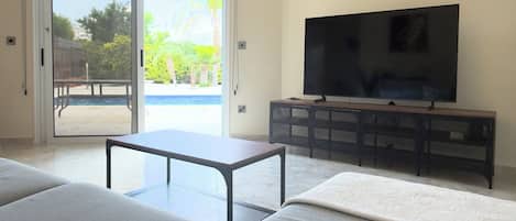 A living room with a sofa, a coffee table, a TV on a stand, and a sliding glass door leading to an outdoor area.