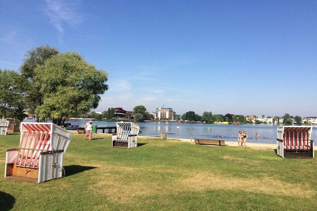 Ein Park am Seeufer mit Liegestühlen, einem Picknicktisch und Blick auf einen See sowie Gebäude in der Ferne.