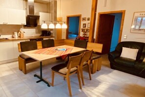 Een eetgedeelte met een tafel, stoelen en een zwarte leren bank.