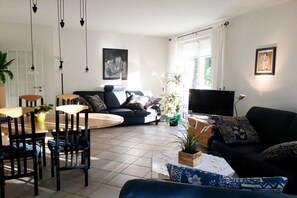 A modern living room with a sofa, TV, and dining area with chairs and a table. - Carpe Diem Lake Park (Seebad Heringsdorf)