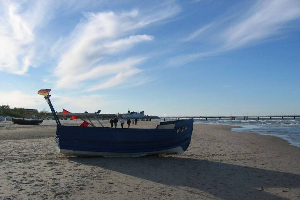 A boat on a sandy beach with a pier in the background.