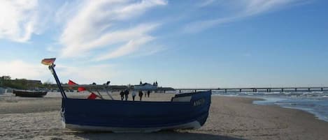 Un bote sobre una playa arenosa con un muelle al fondo.