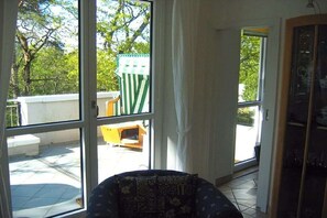 Een kamer met een groot raam, een gestreept sofa en uitzicht op een buitengebied met een groen-witte streepstoel.